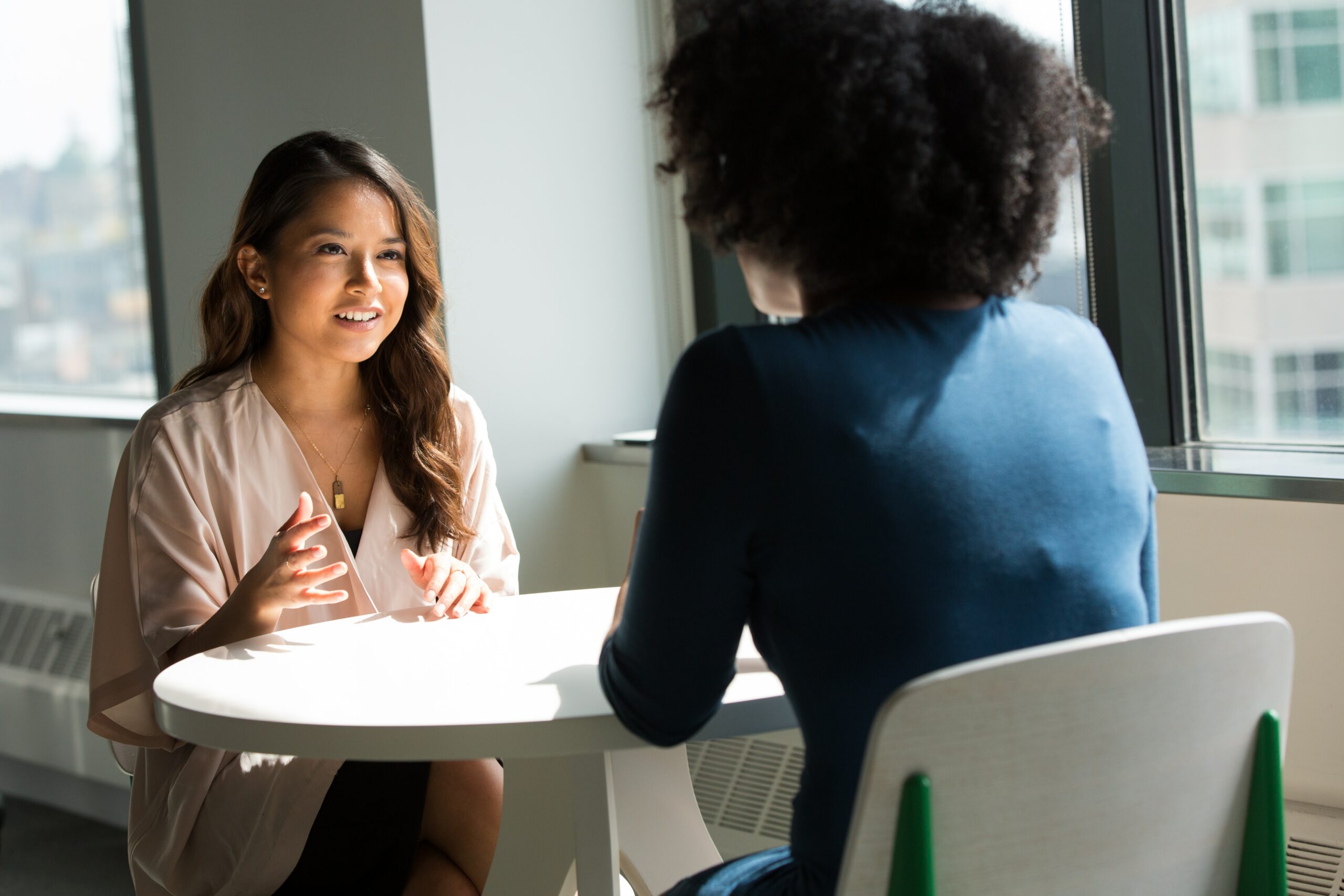 Two women at a table speaking to one another.